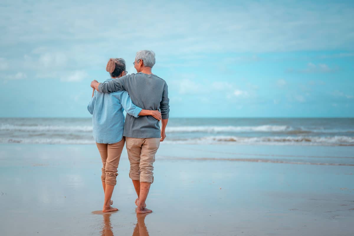 Older couple walking barefoot on the beach.